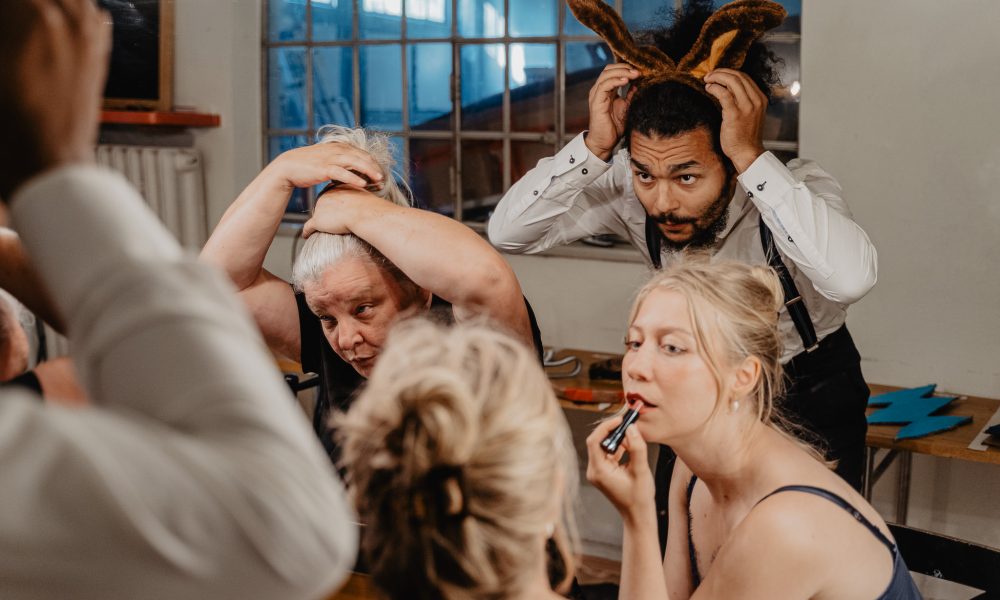 Schauspieler:innen vor dem Spiegel, eine schminkt sich