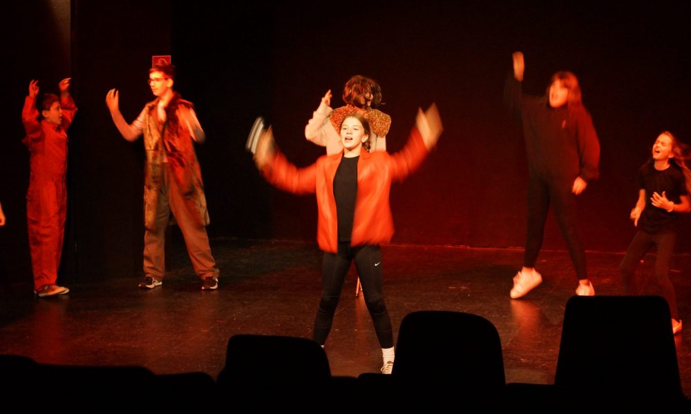viele junge Schauspieler:innen in roter Kleidung, tanzen, singen und springen